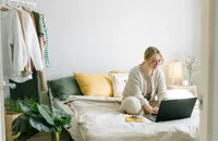 Une femme travaillant à distance assise sur son lit.