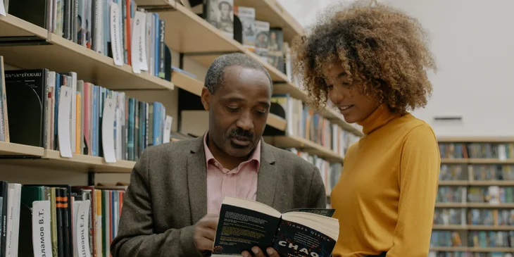 A research consultant working in a library alongside a research intern.