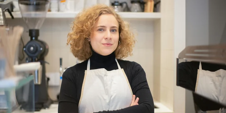 A woman wearing an apron working in a coffee shop.