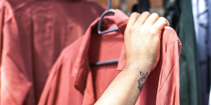 A person holding a red shirt on a hanger in a retail store.