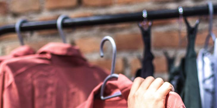 Person holding a red shirt on a hanger in a retail store.