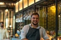 Ein lächelnder Kellner lehnt sich an die Theke einer Hotelbar.