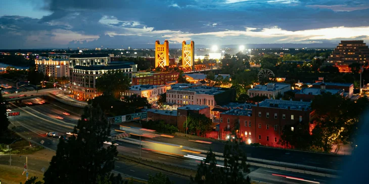 A time-lapse photograph of moving cars on a city road near concrete buildings at night in Sacramento, CA.