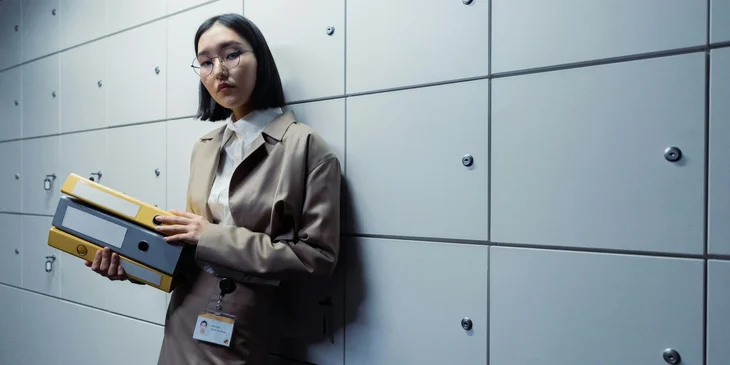 A woman standing by the file storage, holding folders.