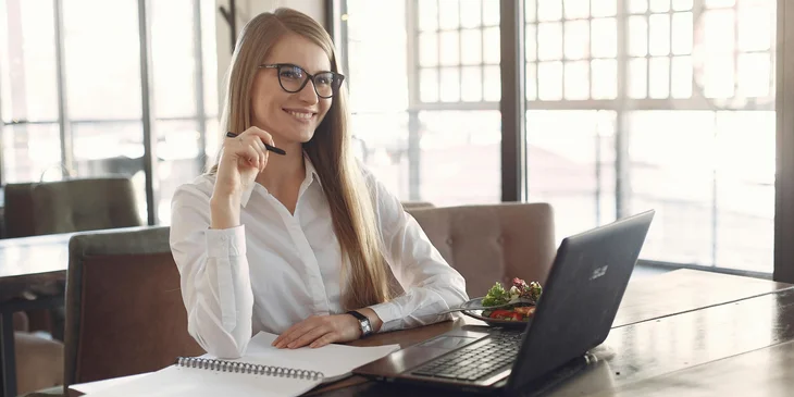 A cheerful young woman with a laptop and notebook in a cafe.