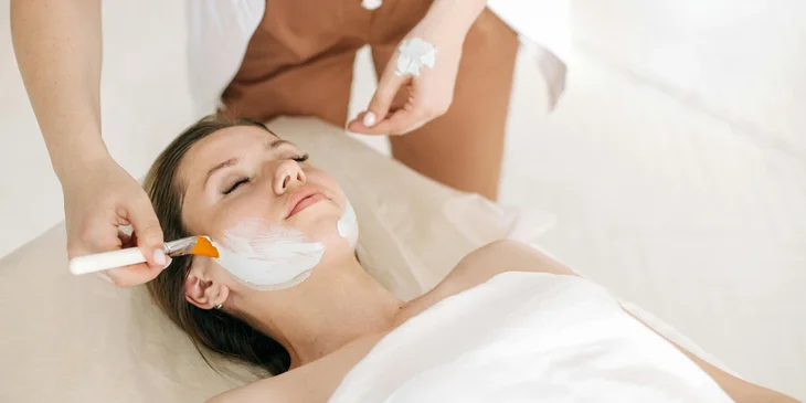 A skincare specialist applying a facial mask to a patient's face.