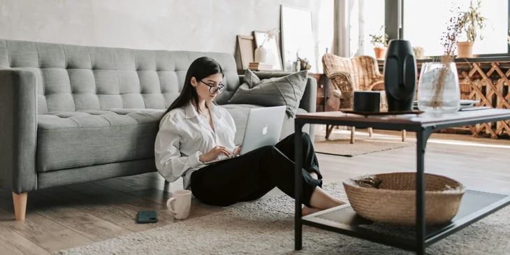 A woman sitting on the floor with her laptop, working from home.