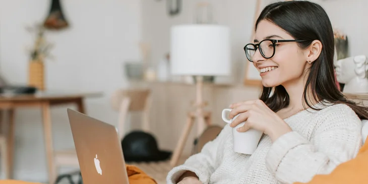 A woman holding a cup of coffee while browsing her laptop.