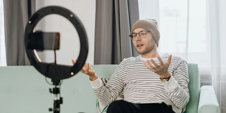 A social media specialist recording a vlog using his cellphone and a ring light.