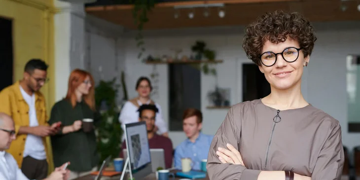 A smiling woman with her arms crossed, with coworkers behind her.