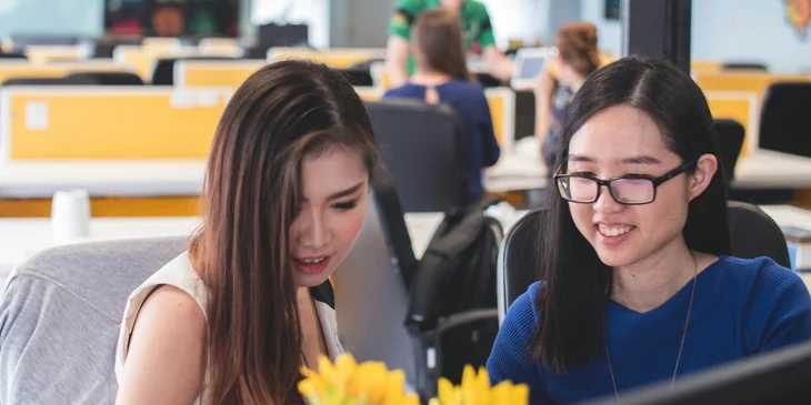 Two smiling women working on a computer together.