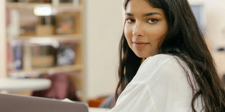 A woman in a white long sleeve shirt using a silver laptop.