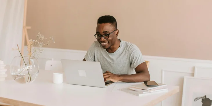A man in a gray crew neck shirt using a laptop.