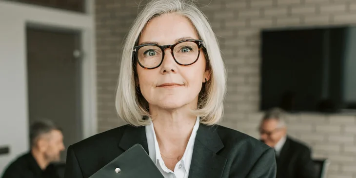A woman in a black blazer holding a black clipboard.