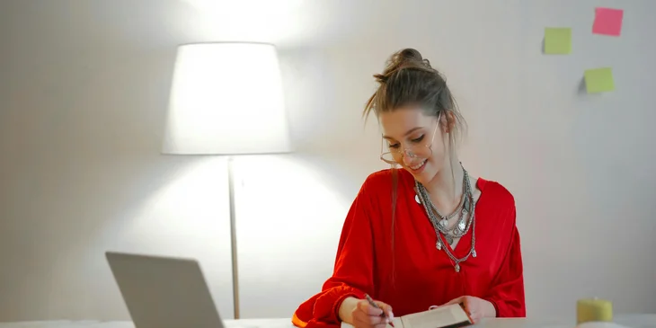 A woman writing in a notebook on her desk.