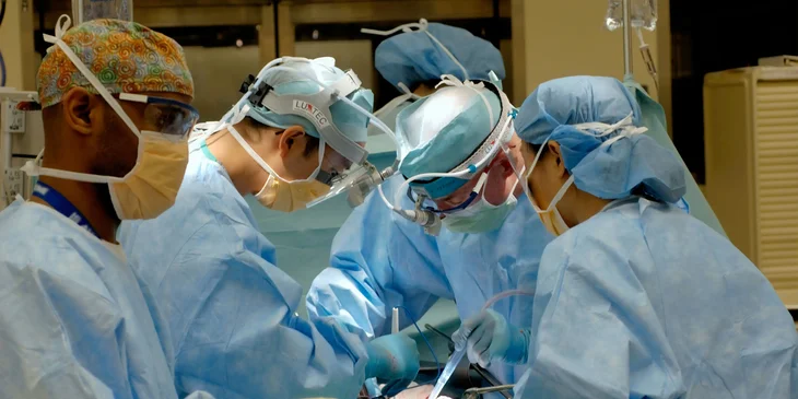 A thoracic surgeon, along with other surgeons, participates in a heart transplant procedure.