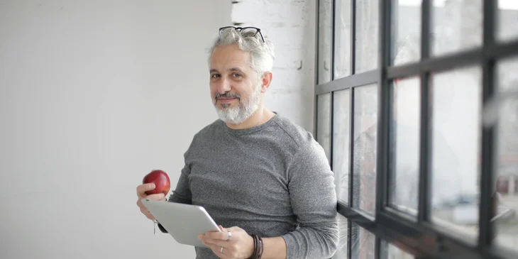 A teacher holding an apple and a tablet.