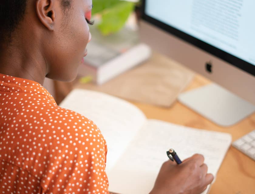 A transition manager writing in a notebook at a desk with a computer.
