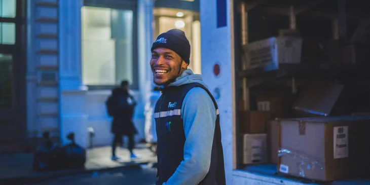 A smiling man stands behind a delivery truck.