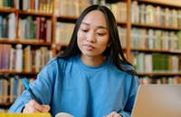 Una studentessa che studia al pc e sottolinea dei libri.