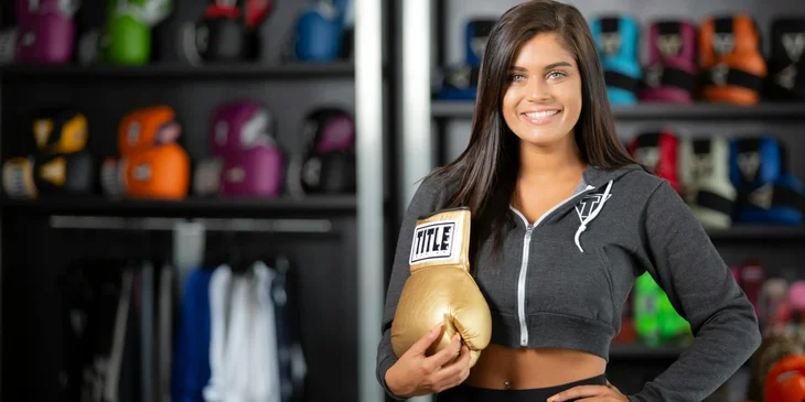 A woman holding a gold boxing glove while smiling at the camera.