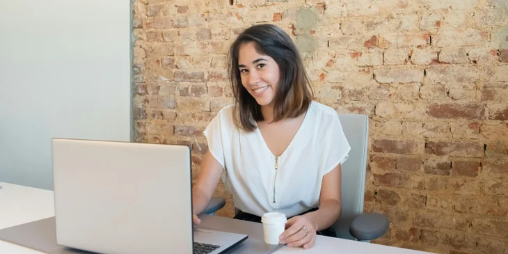 A woman in a white top using her laptop while smiling.
