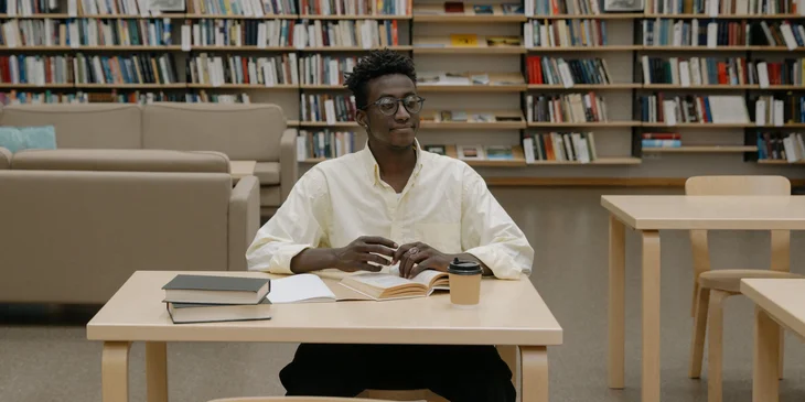 A student in a white shirt sitting on a chair inside a library.