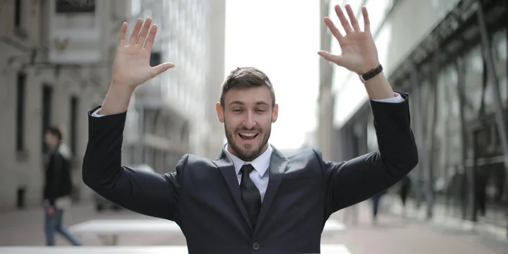 A man in black suit raising both hands.