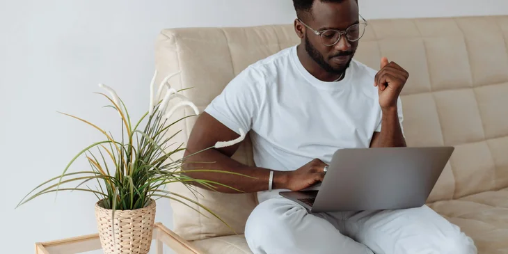 A man sitting on a couch while working on his laptop.