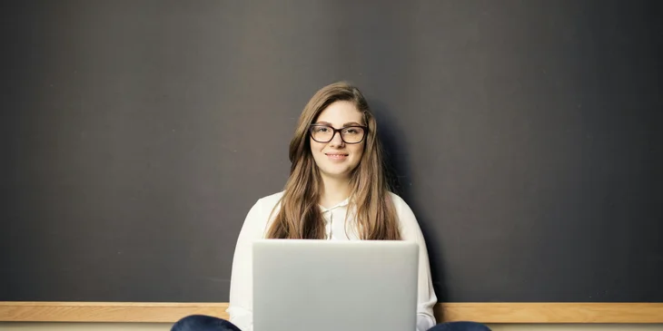 A woman sits on the floor with a laptop.