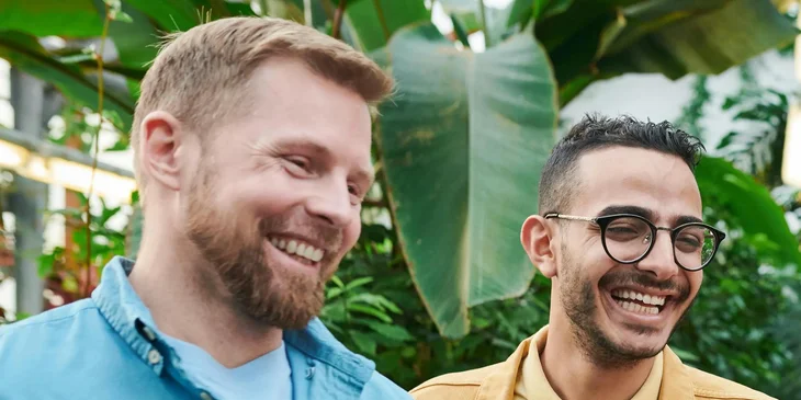 Zwei Mitarbeiter stehen vor einem Palmenblatt in dem Garten eines Büros.