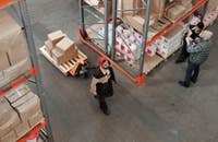 Un Clasificador de Almacén traslada paquetes de un lugar a otro mientras dos compañeros discuten sobre su trabajo.