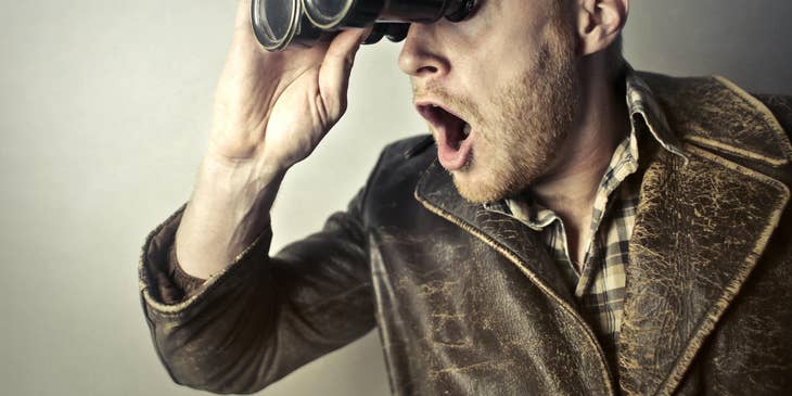 Man in a leather jacket using binoculars to search for something