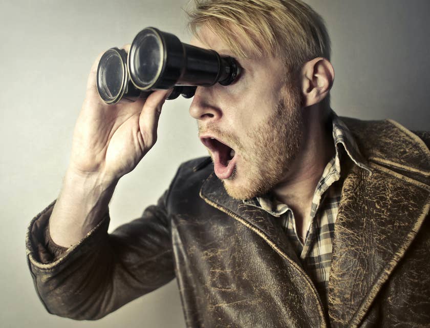 Man in a leather jacket using binoculars to search for something