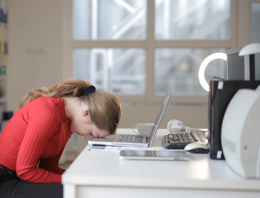 employee in red and black resting forehead on laptop