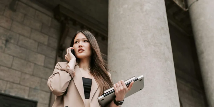A woman talking on her mobile phone and carrying a laptop in her other hand.