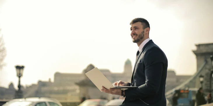 A man sitting outdoors with a laptop in his hands.