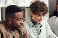 Zwei Menschen arbeiten gemeinsam auf einem Laptop.