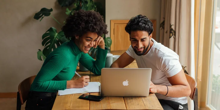 A man and a woman reviewing a document on a laptop.