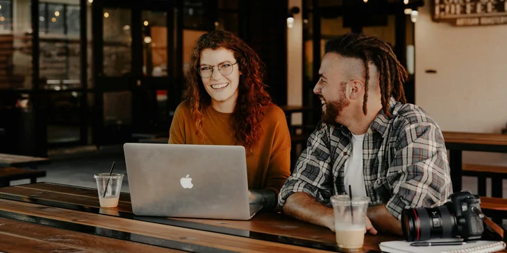 A man and a woman sitting in front of a silver laptop.