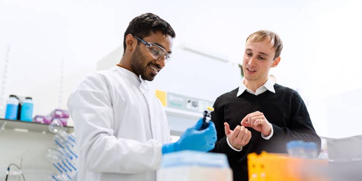 Biochemical Engineer conducting research in a laboratory and showing a vial to his assistant