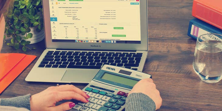 Bookkeeper using calculator besides an open laptop.