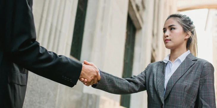A business development executive shaking hands with the newly procured client after a meeting.