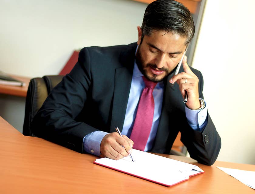 A Business Lawyer in an office reading a book while talking with a client on the phone.
