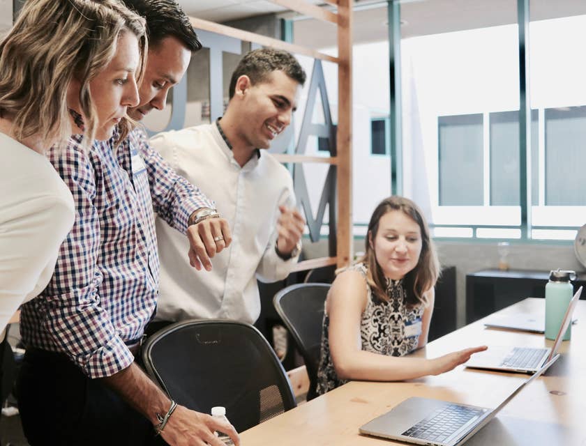 Business Systems Analyst showing something to her colleagues while they lean on and look at her laptop