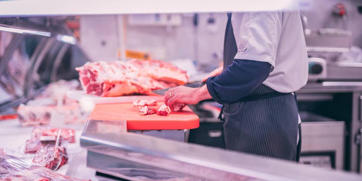 Butcher slicing raw meat as of customer's preference.