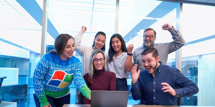Call Center Manager celebrating with her team in the office after presenting the report on her laptop