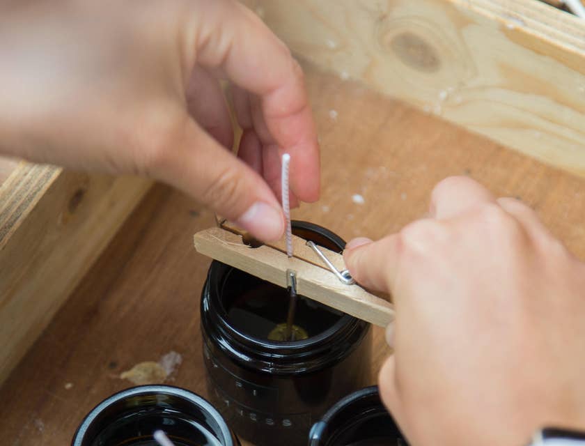 A Candle Maker dipping and preparing candle wicks inside the glass molds filled with molten wax.