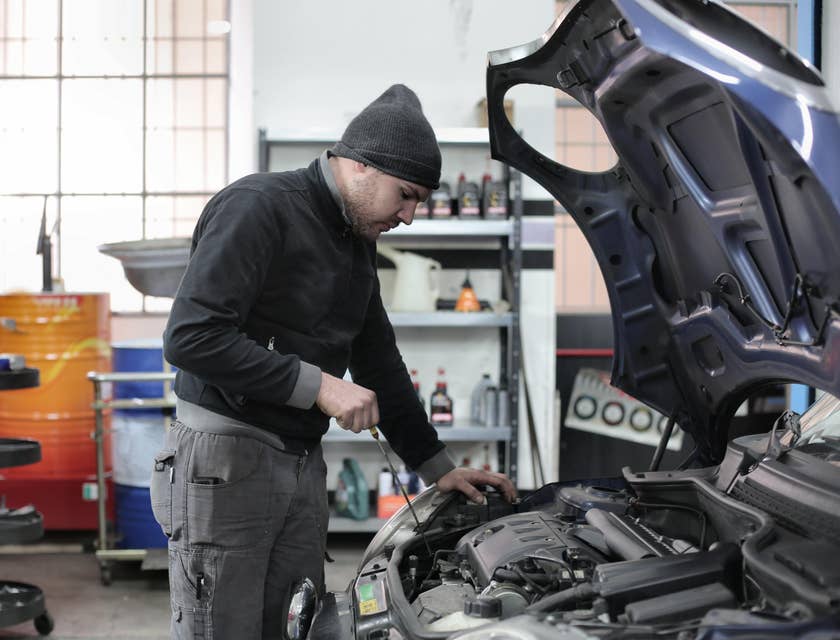 A Car Porter in an automotive workshop holding a dip stick to ensure oil is sufficient or needs to be refilled.