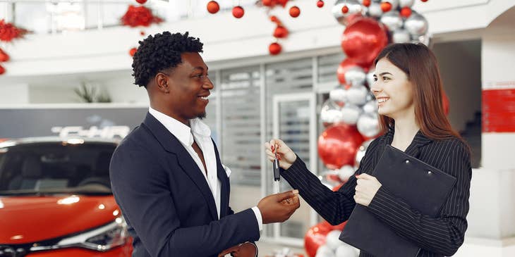 Car Salesman handing over the key to the client after a successful purchase of a brand new car